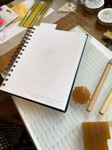 A sketchbook with a drawing of a pendant, and the partially carved wax model for the pendant.