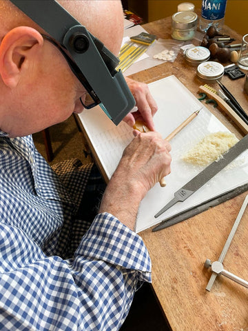 A jeweler wearing a magnifying visor is carving wax to make jewelry.