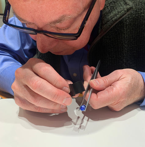 A jeweler looking through a loupe at a blue gemstone