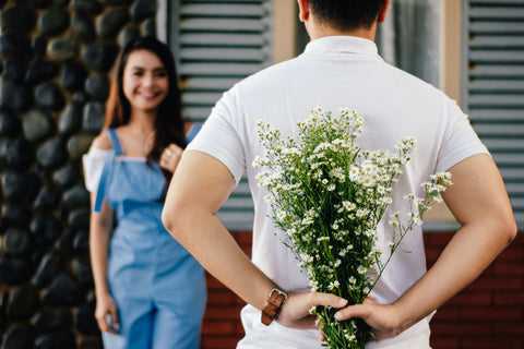 Man holding flowers behind his back in front of woman