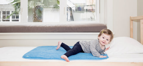 young girl laying on top of PeapodMats on a bed