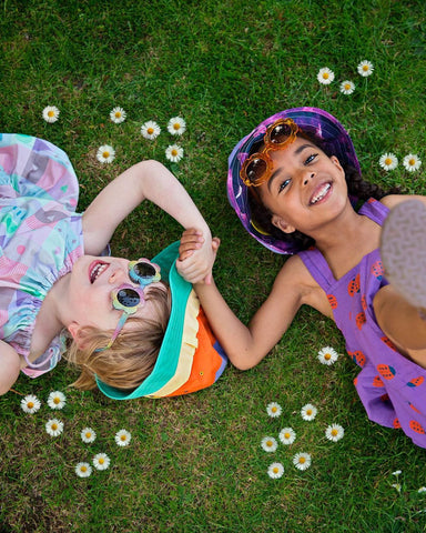two girls holding hands lying on grass with hats on 