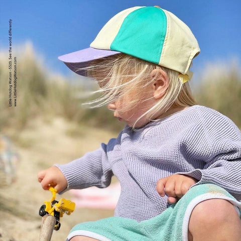 toddler on beach playing with toy in pastel baseball cap