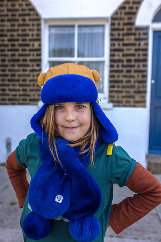 Child wearing blue scarf and cinnamon and blue winter trapper hat