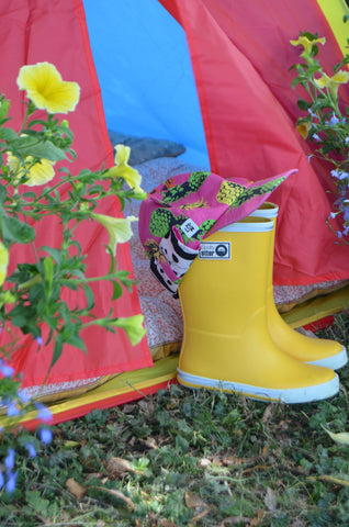 Yellow kids wellies with a pink hat perched on top in front of a tent