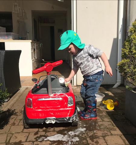 Child washing a large toy car wearing a turquoise hat