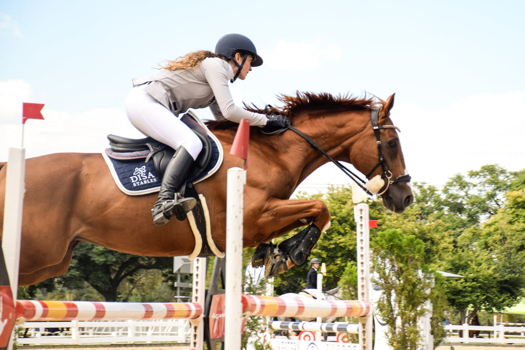 A woman jumping her chestnut horse wearing Scoot Boots over a 1.25 metre jump