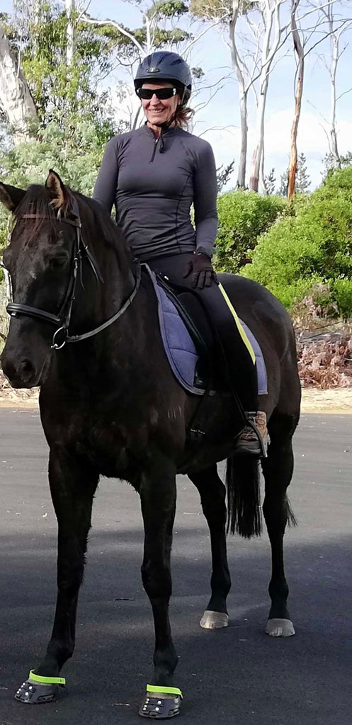 A woman riding a black horse wearing green and black Scoot Boots on a trail ride