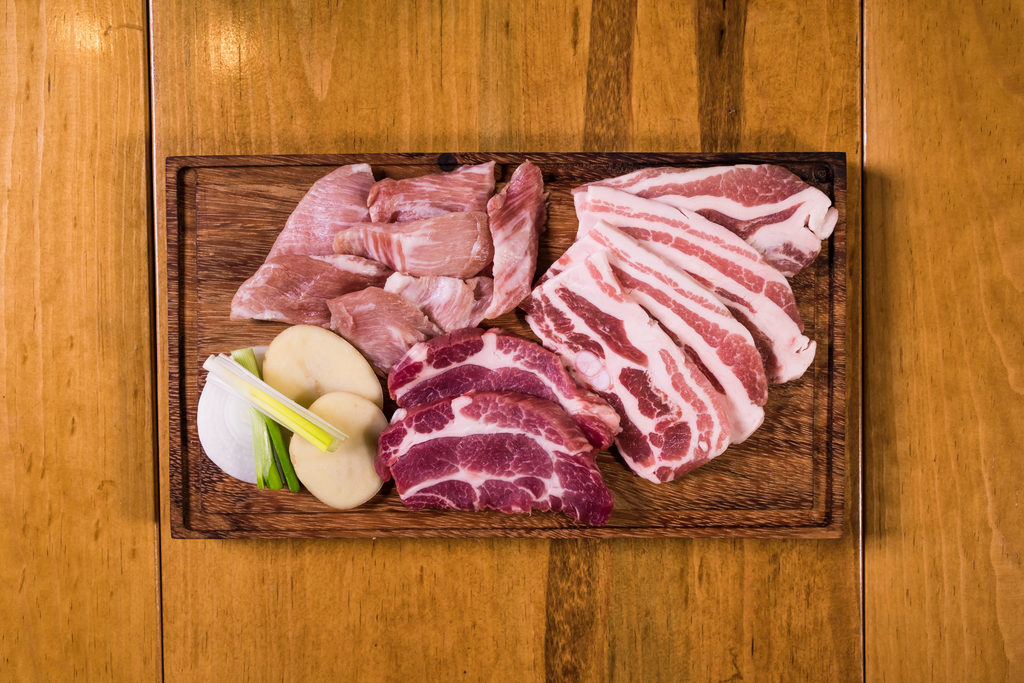 A vegetable and raw meats on a cutting board.