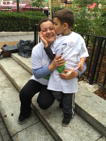 A photo of a young boy kissing his mom and holding her face while at a clean up event, both wearing UP-STAND supporter pins