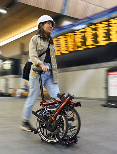 Gefaltetes Brompton Fahrrad wird am Sattel durch Flughafen geschoben