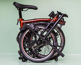 Gefaltetes Brompton Faltrad der Farbe Flame Laqcuer vor grünem Hintergrund