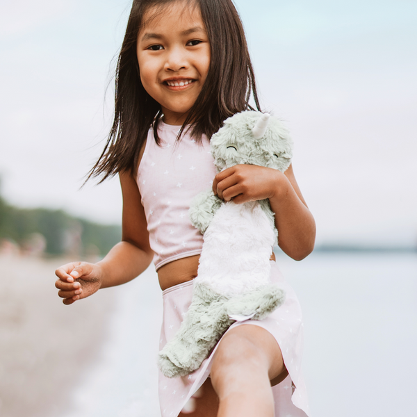 Child on a beach holding Narwhal Snuggler