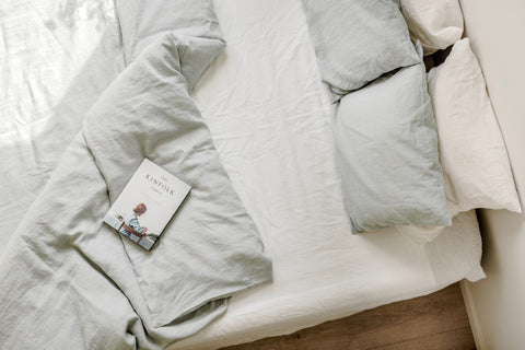 An empty bed with the sage green linen duvet pulled back and a book lays waiting for them to return.