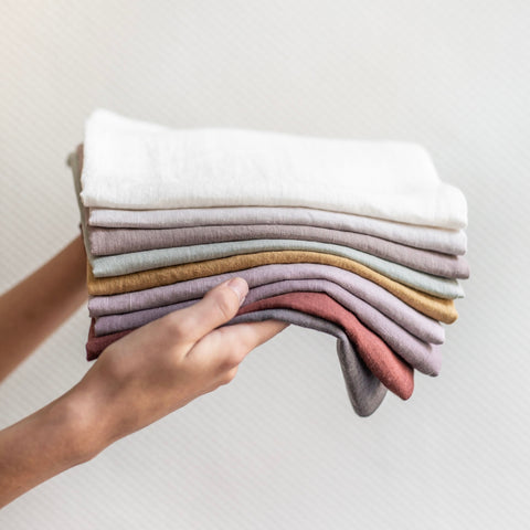 Two hands holding a stack of fine linen napkins, in a range of soft colours
