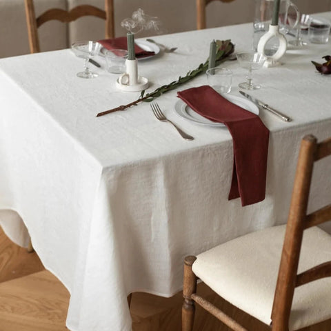 A rustic table dressed with white linen tablecloth. A long thin terracotta napkin hangs across each plate and over the edge of the table.