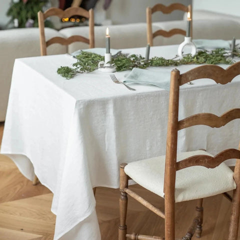 A white linen tablecloth on a rectangular table with rustic ladder back chairs.  