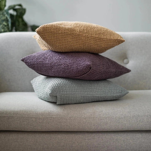 Three Linen & Letters waffle linen cushion covers stacked on a grey sofa.