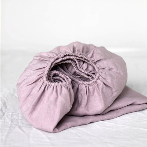 Dusky rose fitted linen sheet folded on a bed.