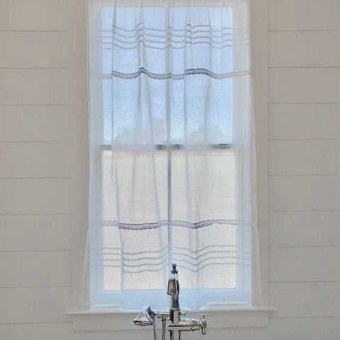 A Linen and Letters sheer white curtain hangs over a tall bathroom window.