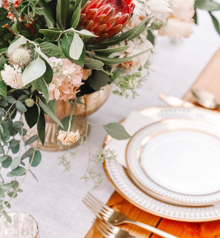 A luscious wedding table with an exquisite floral centrepiece, white gilded plates and a fine linen runner in the centre.