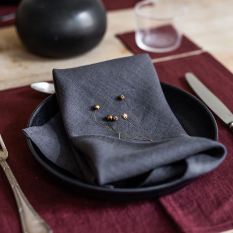 Charcoal gray linen napkin, folded on a black plate with a decorate floral sprig.
