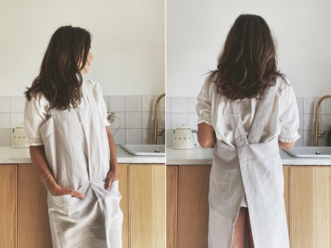 A woman casually leaning against a kitchen counter in a linen apron. A woman work in a kitchen with her back to us, showing the crossed straps of the cross backed apron.