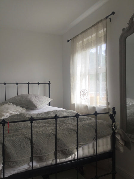 Grey cast iron bed next to a window draped in dreamy sheer linen curtains embroidered with a large monogram.