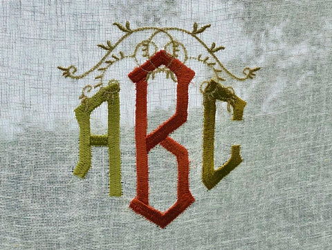 A close up of a natural linen curtain embroidered with a three letter monogram. The three letters are embroidered in autumn colours and styled to mimic a pumpkin.