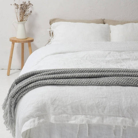 Beautiful bed with bright white linen sheets. A grey waffle throw lays across the bottom of the bed.