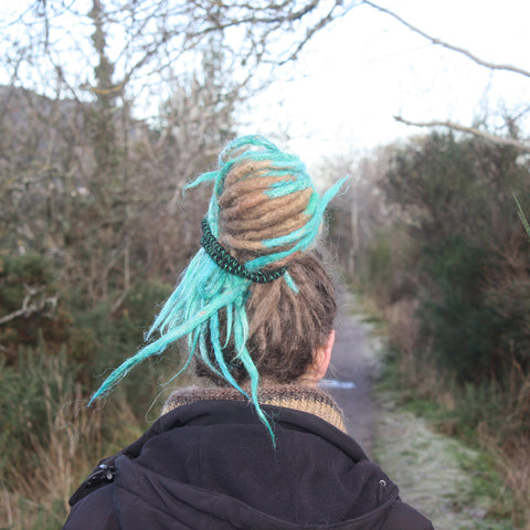 girl with dreadlocks walking away down a path with her hair tied up with a spiral hair tie