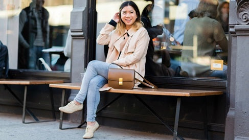 woman sitting on a bench wearing a beige jacket, denim pants and beige shoes