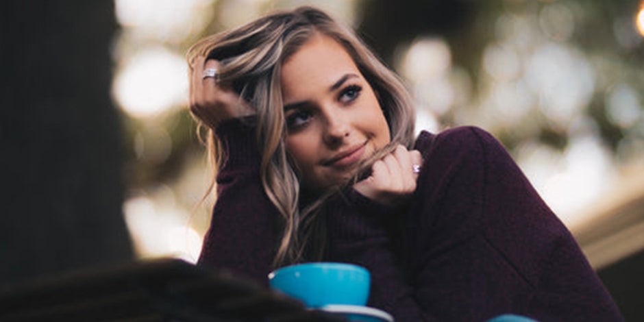 Girl wearing purple sweater with a blue cup of coffee infront of her