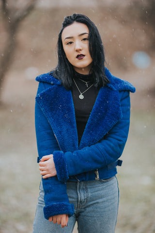 a woman in a blue jacket and jeans standing in the snow
