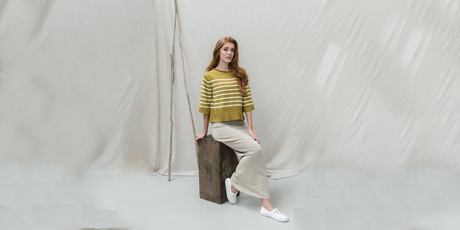 arafed woman sitting on a wooden block in front of a white backdrop