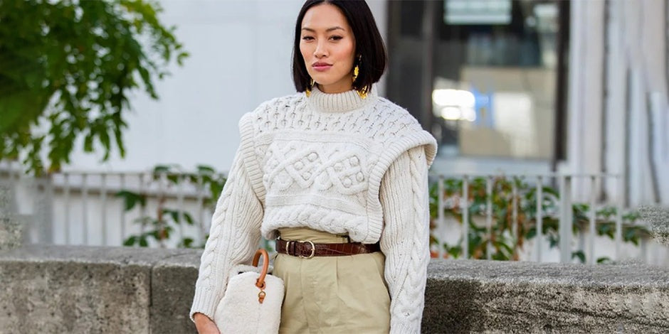 araffe woman in a white sweater and khaki pants standing on a stone wall