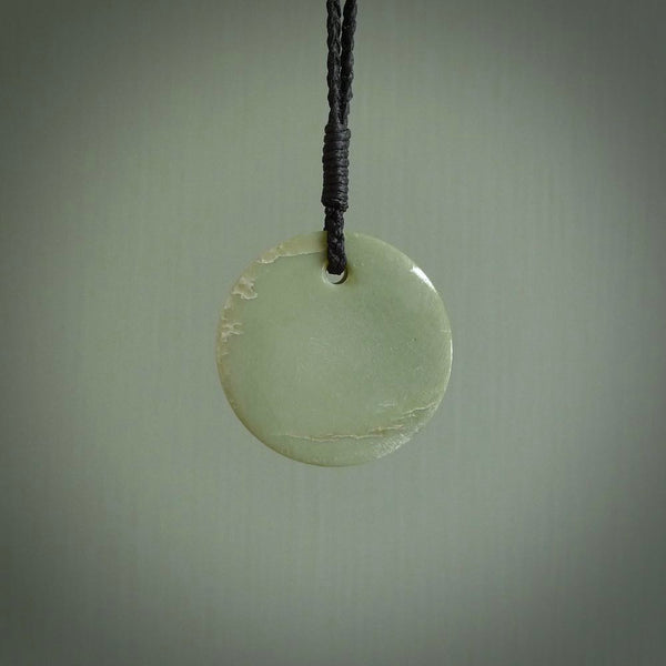 This piece is a small sized, oval round, disc pendant. It was carved for us by Alex Sands from a lovely light green piece of New Zealand Inanga jade. It is suspended on a black coloured braided cord that is length adjustable.