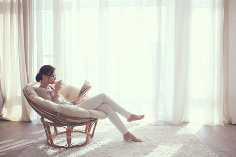 Woman sitting in chair reading a book with cup of tea