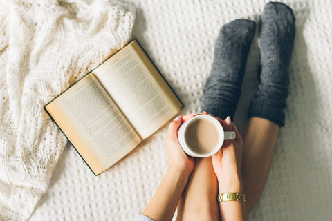 Woman lying in bed reading a book with a cup of coffee