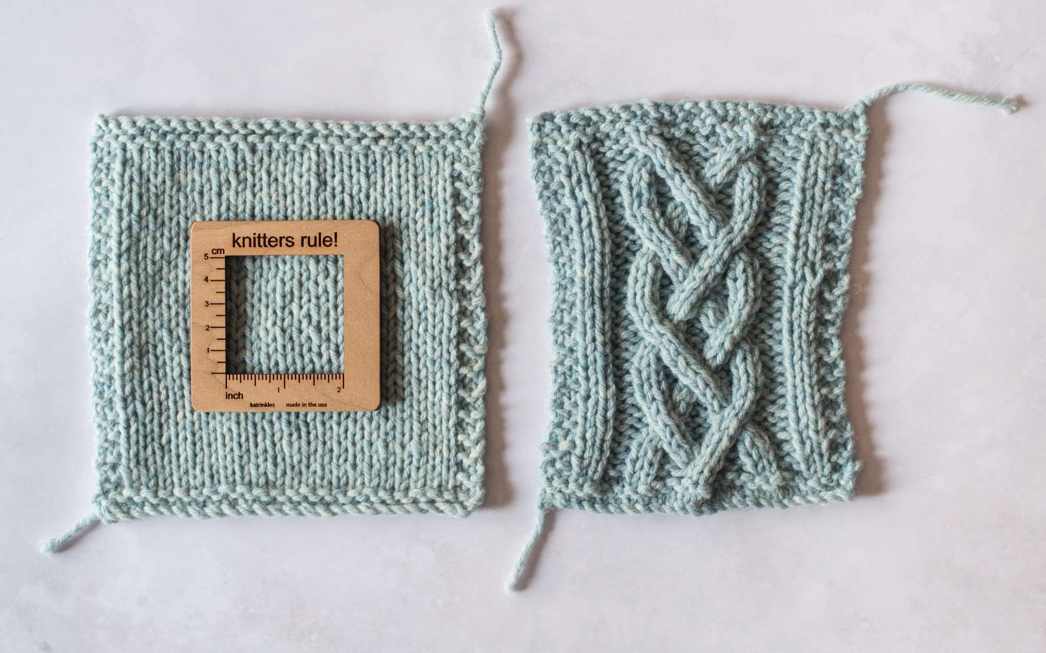 Two swatches lie next to each other. The left swatch has been knitted in stocking stitch and has a wooden measuring tool on top. The swatch in the right is in the same yarn but has been knitted in a more dense cabled pattern.