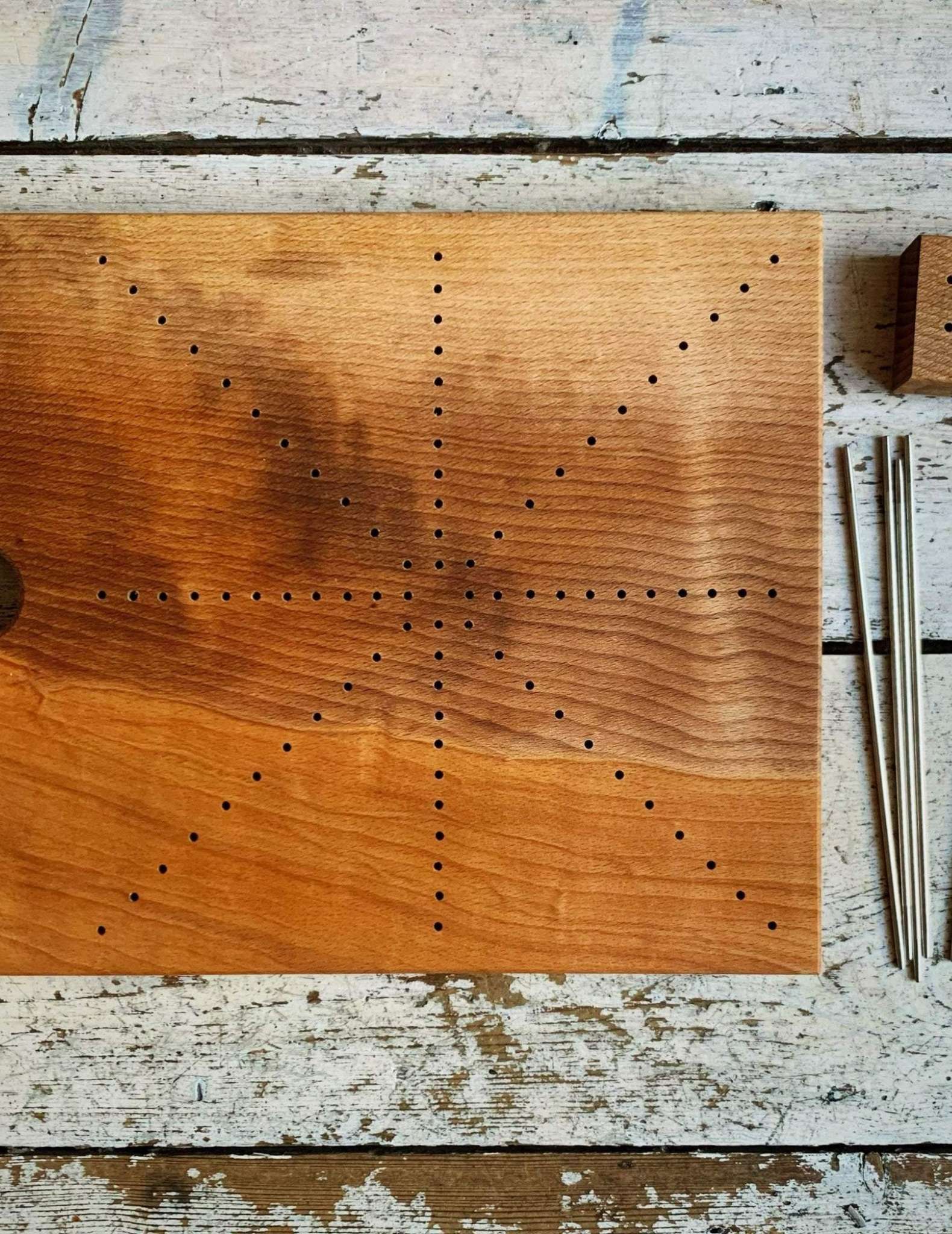 A wooden board marked with holes in diagonal lines over the surface, with blocking pins laying at the right side.
