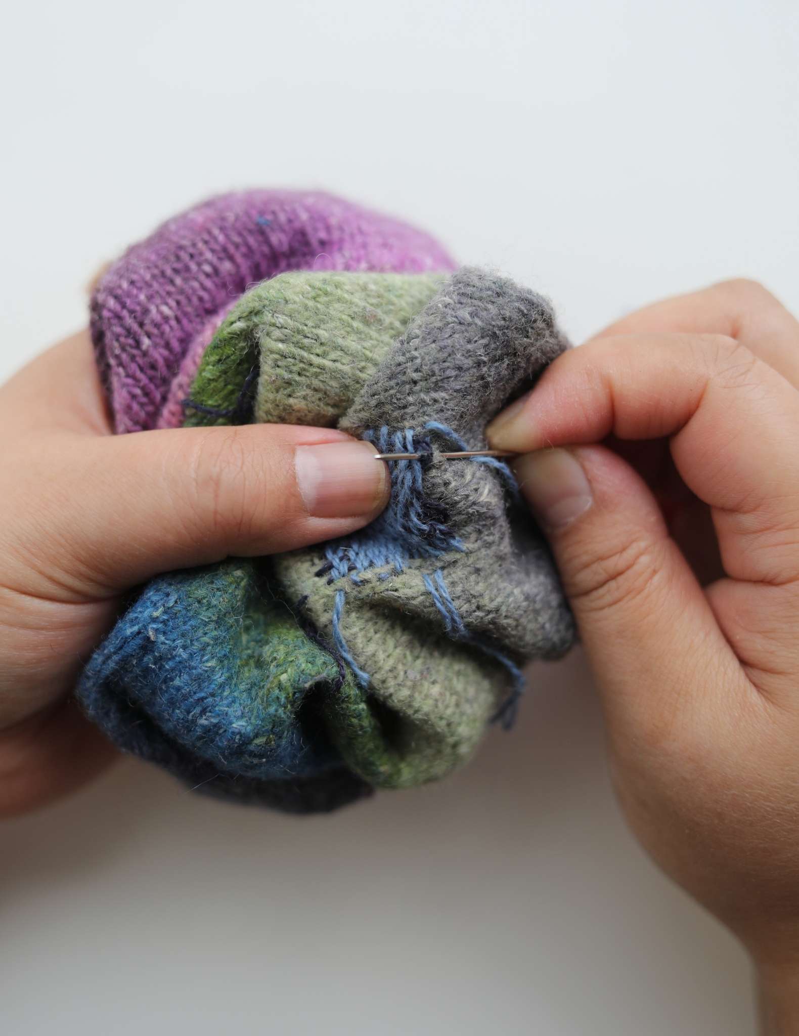 The sock has been scrunched up and the darning loom removed. Hands hold the sock near the patched hole and the right hand is hand stitching the top of the darned area.