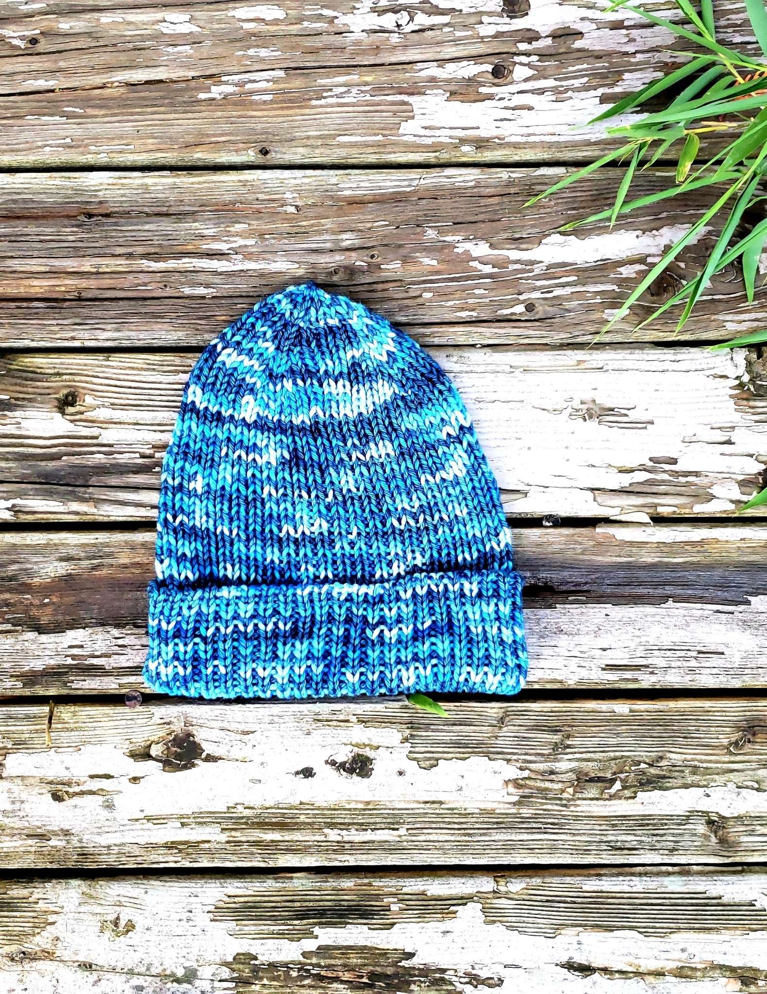 A variegated bright blue ribbed hat is photographed on a worn wood floor.