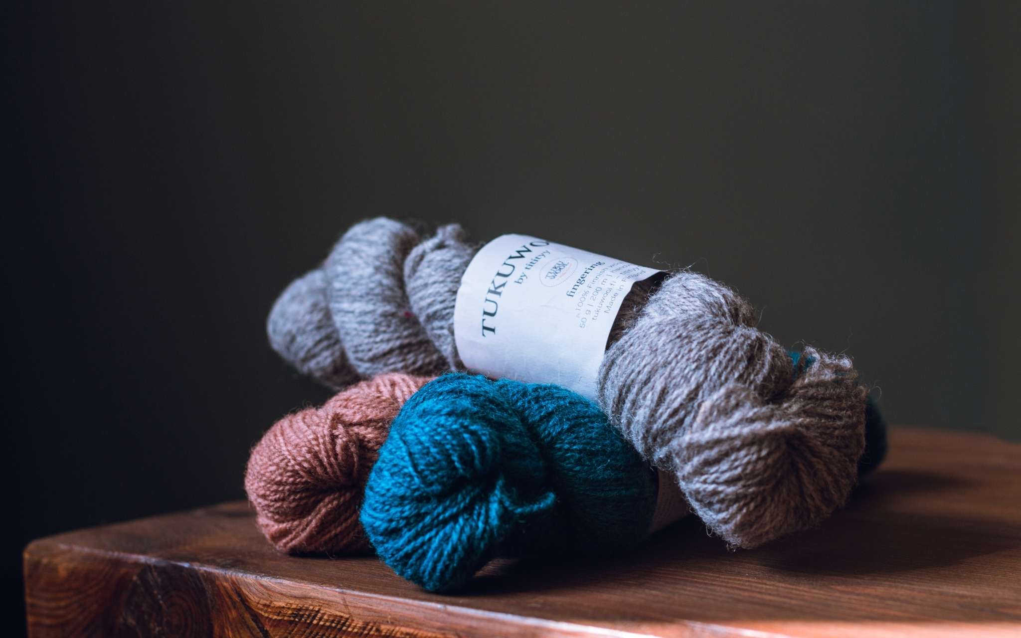Three skeins of yarn in grey, blue and coral lie piled on top of each other on a table.
