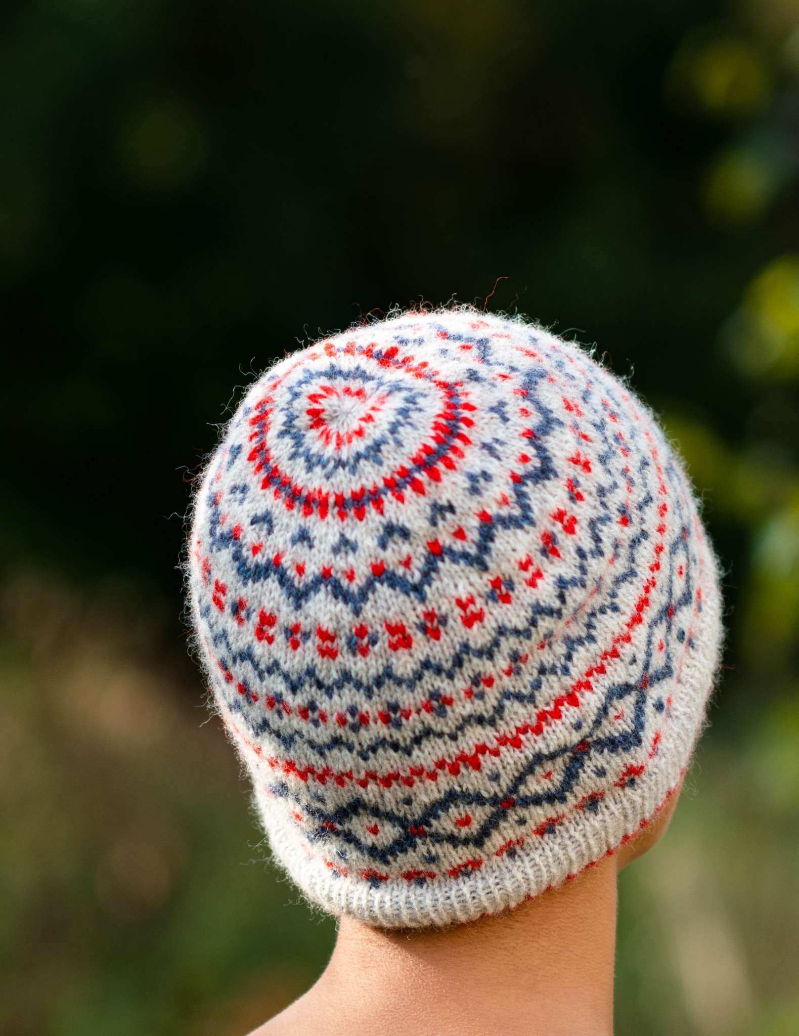 a model wears a colourwork beanie hat in cream, red and blue and faces away from the camera