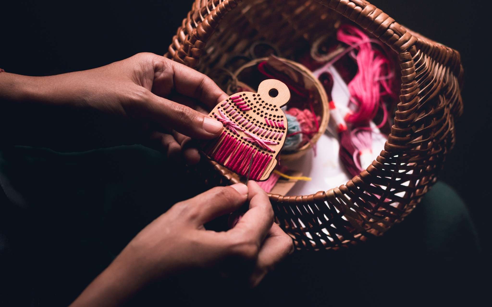 A hat shaped wooden tree ornament is held in hands as it's stitched with brightly coloured threads.