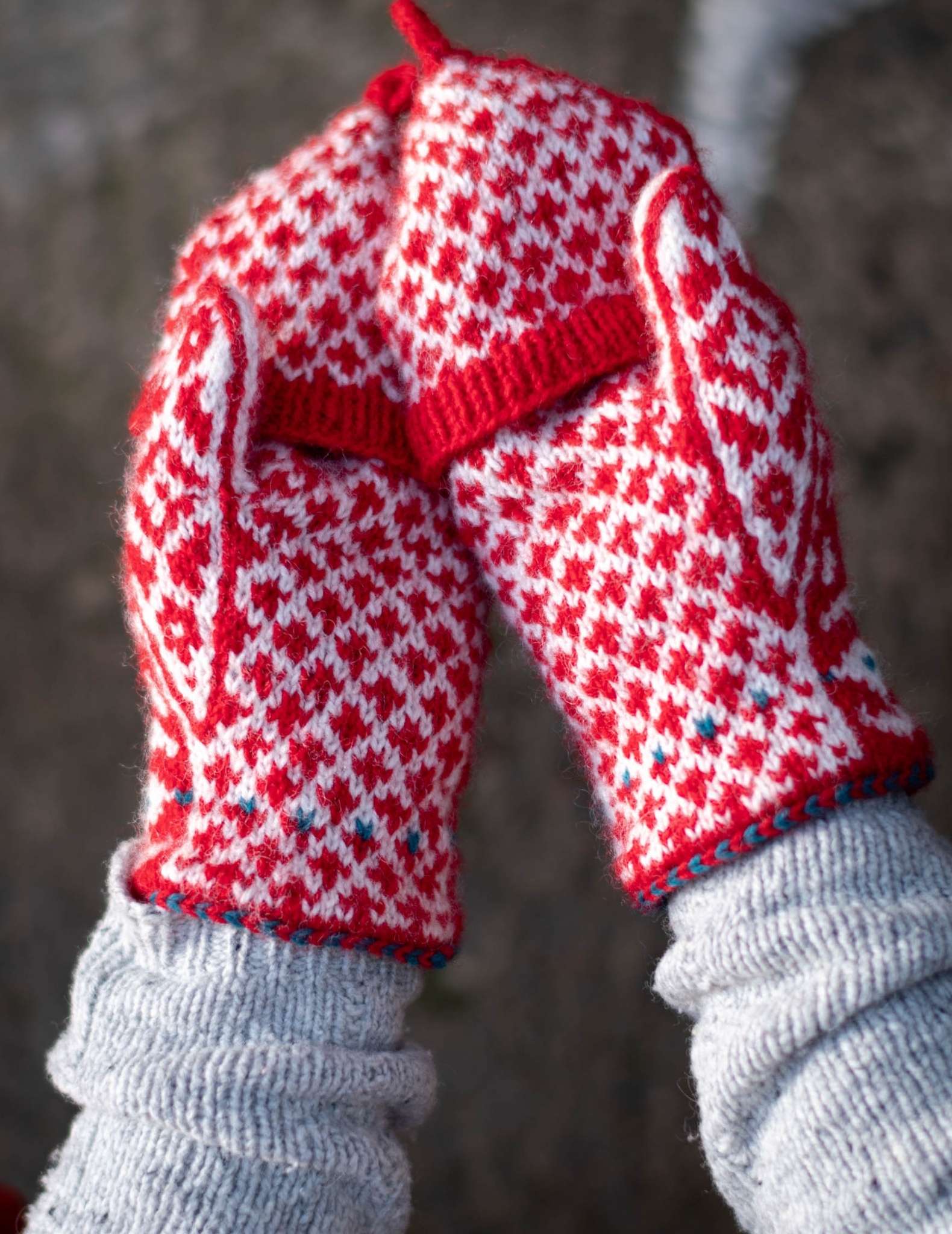 Hands wear a pair of colourwork mittens in red and white, and are held side by side with the palms facing up.