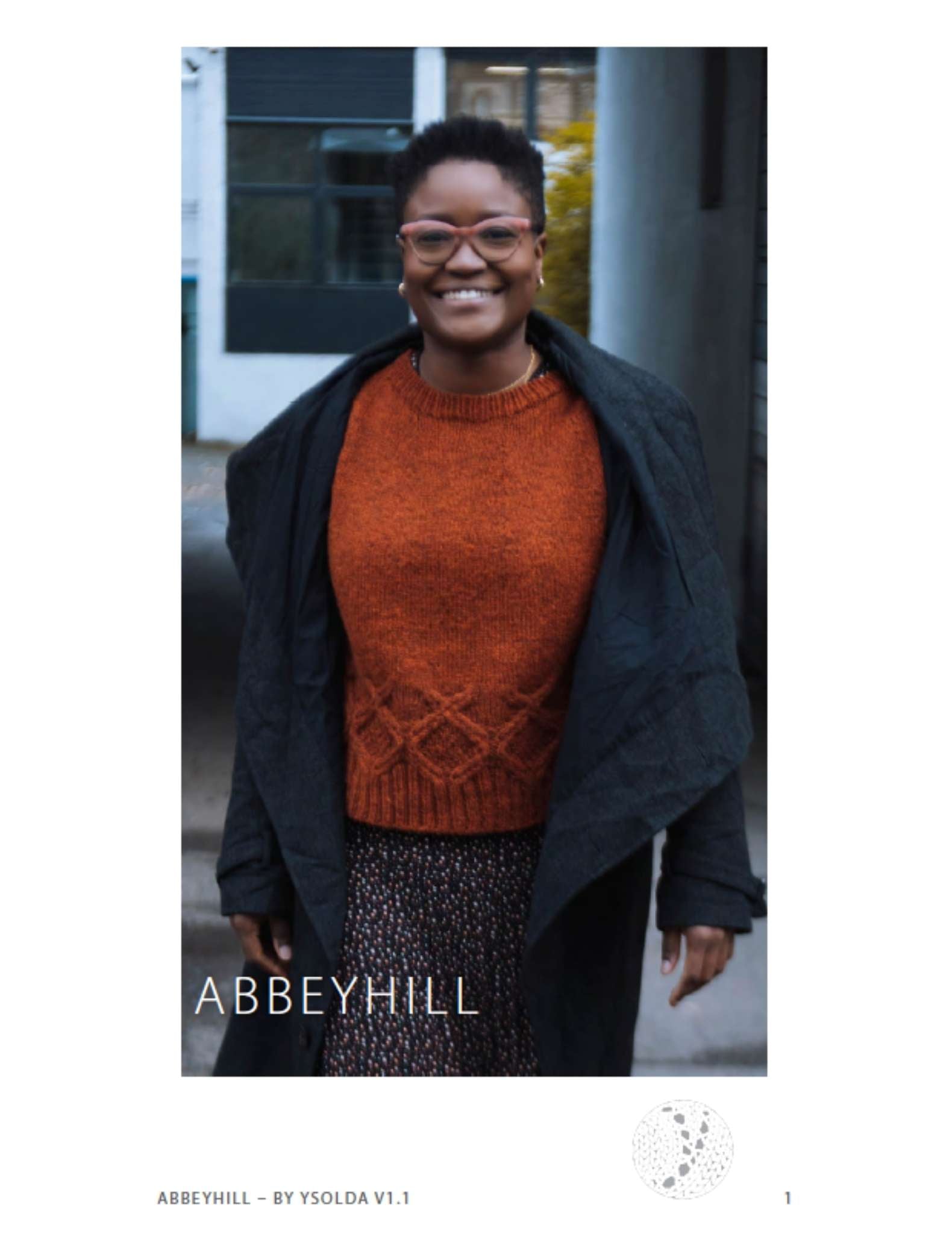 image of a black woman wearing an orange sweater and open, dark jacket. She is walking towards the camera and smiling.