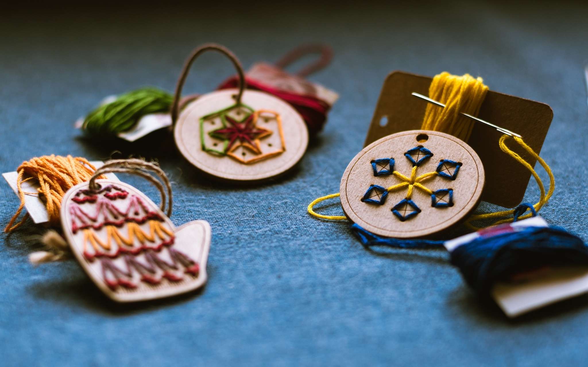 Wooden hanging ornaments shaped as mittens, a circle and a snowflake have been hand stitched through holes in the wood with brightly coloured threads.
