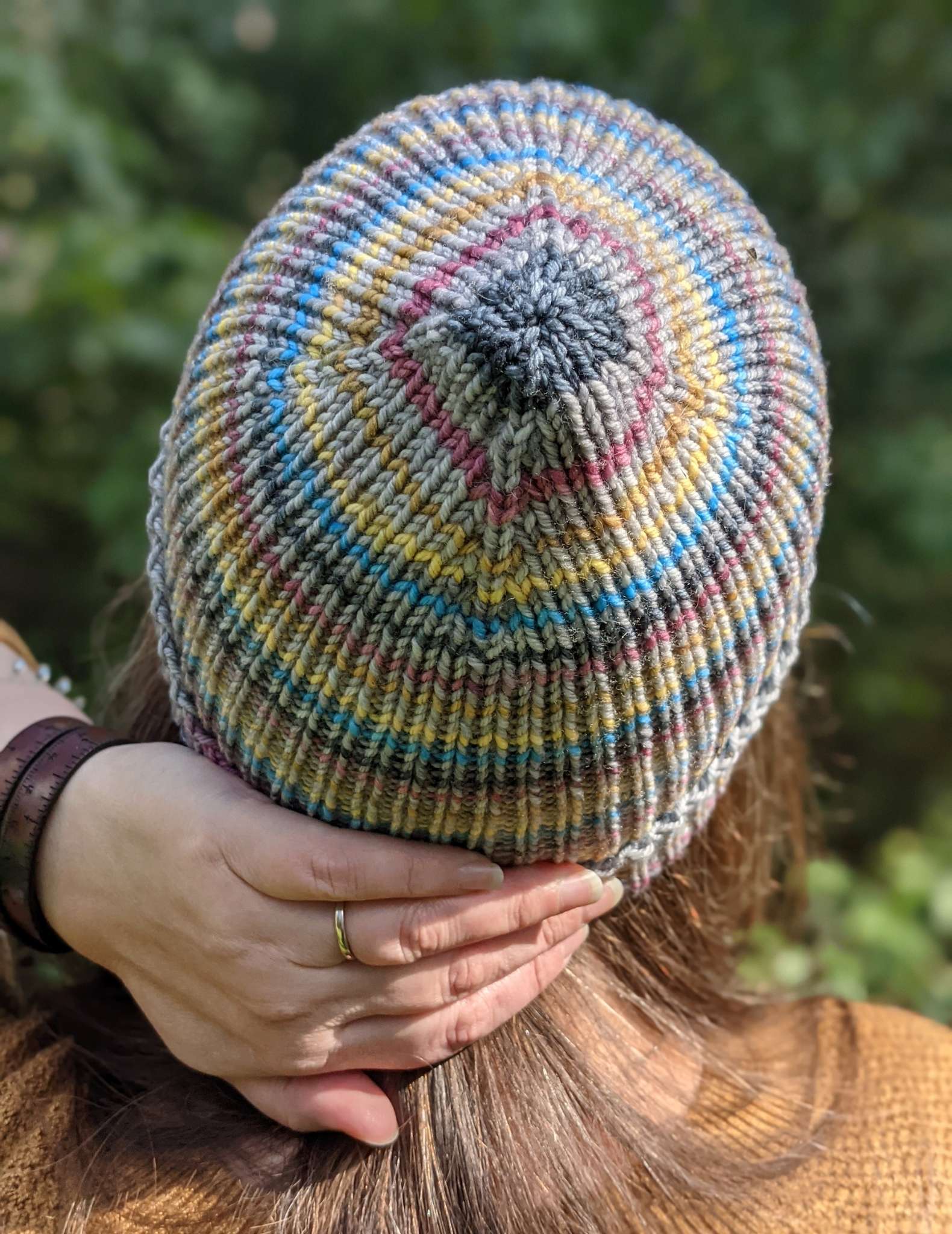 Close up of the crown of a striped hat pictured from behind. The narrow stripes are grey, charcoal, plum, yellow and bright blue.